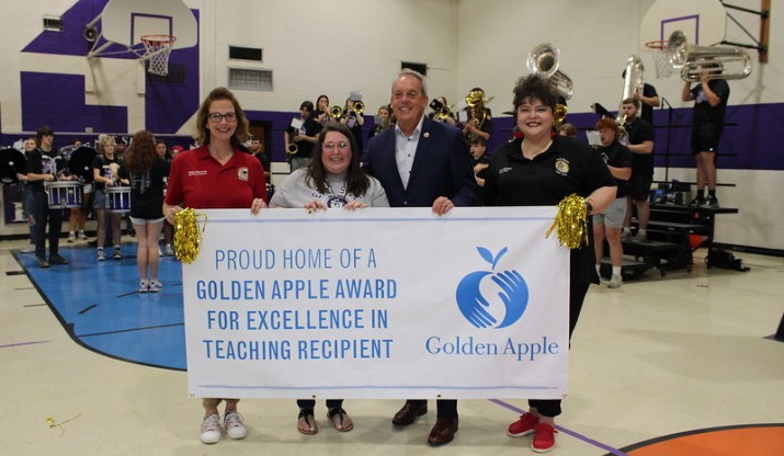 Illinois College alumna Christina Beck '04 posing at school with Golden Apple banner